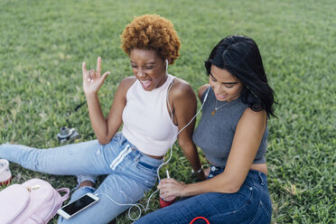 Zwei glückliche Freundinnen entspannen sich in einem Park und hören Musik - BOYF01187