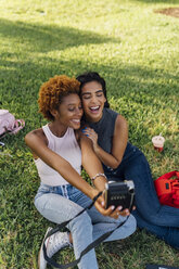Zwei glückliche Freundinnen machen ein Sofortfoto in einem Park - BOYF01200