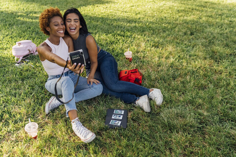 Zwei glückliche Freundinnen machen ein Sofortfoto in einem Park, lizenzfreies Stockfoto
