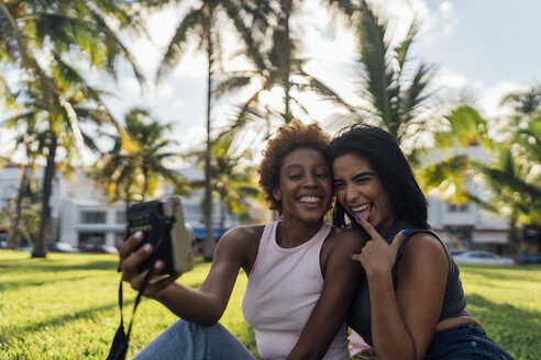 Zwei glückliche Freundinnen machen ein Sofortfoto in einem Park - BOYF01202