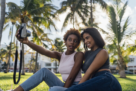 Two happy female friends taking an instant photo in a park stock photo