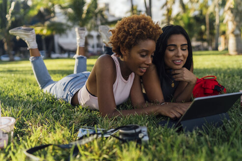 Zwei Freundinnen entspannen sich in einem Park und benutzen ein Tablet - BOYF01211