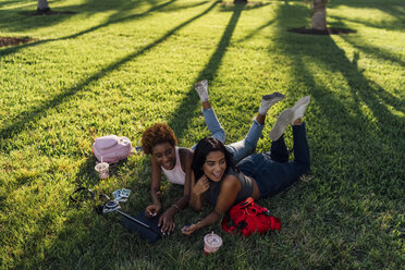 Zwei glückliche Freundinnen entspannen sich in einem Park und benutzen ein Tablet - BOYF01213