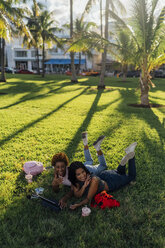 Zwei glückliche Freundinnen entspannen sich in einem Park und benutzen ein Tablet - BOYF01214