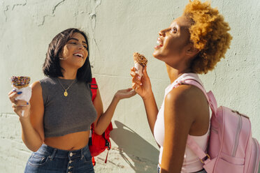 Two happy female friends with ice cream cones at a wall - BOYF01223