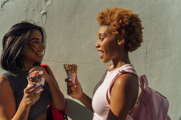 Two happy female friends with ice cream cones talking at a wall - BOYF01225