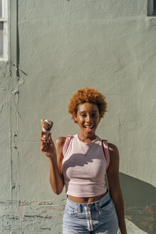 Porträt einer glücklichen jungen Frau mit Eiswaffel an einer Wand - BOYF01226