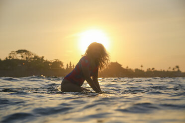 Indonesia, Bali, pregnant woman sitting on surfboard at sunset - KNTF02452