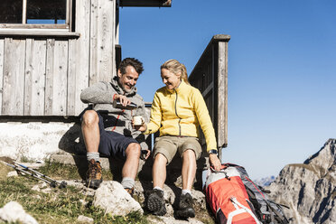 Wanderpaar vor einer Berghütte sitzend, eine Pause einlegend - UUF15962