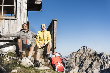 Hiking couple sitting in front of mountain hut, taking a break - UUF15965