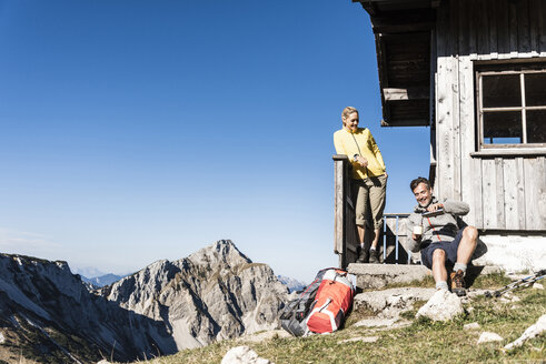 Wanderpaar vor einer Berghütte sitzend, eine Pause einlegend - UUF15966
