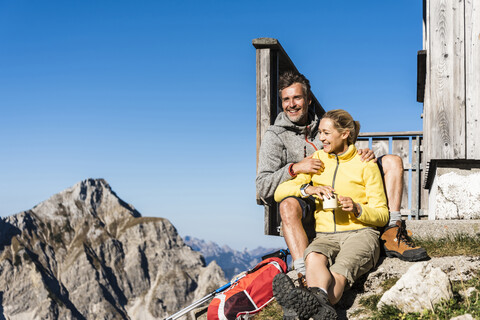 Wanderpaar vor einer Berghütte sitzend, eine Pause einlegend, lizenzfreies Stockfoto