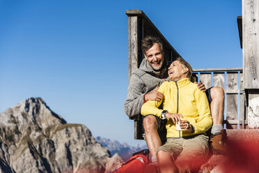 Wanderpaar vor einer Berghütte sitzend, eine Pause einlegend - UUF15970