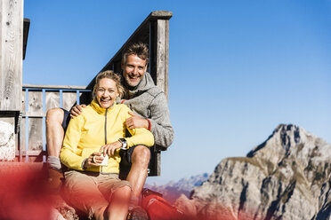 Wanderpaar vor einer Berghütte sitzend, eine Pause einlegend - UUF15971