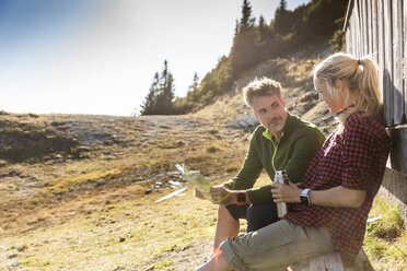 Hiking couple sitting in front of mountain hut, taking a break, holding map - UUF15978