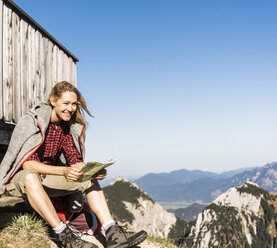 Lachende Frau, die auf einer Berghütte eine Pause einlegt und eine Karte hält - UUF15985