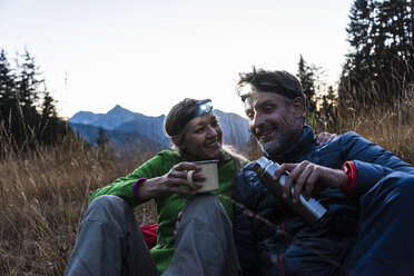 Hiking couple taking a break in the evening, wearing head lamps, drinking tea - UUF16042