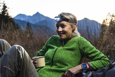 Hiking woman taking a break, drinking tea, wearing head lamp - UUF16044