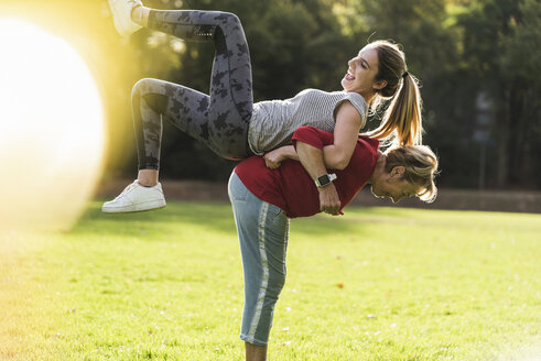 Grandmother lifting granddaughter on her back, having fun in a park - UUF16071