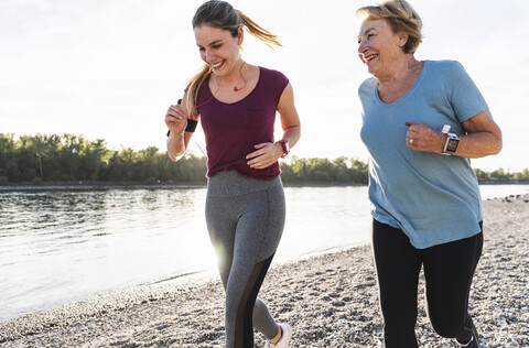 Enkelin und Großmutter haben Spaß, joggen zusammen am Fluss, lizenzfreies Stockfoto