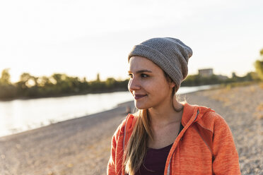 Porträt einer sportlichen jungen Frau am Fluss, die eine Mütze trägt - UUF16118