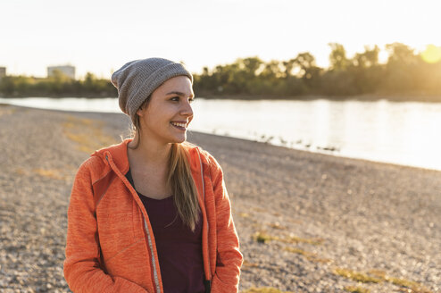 Porträt einer sportlichen jungen Frau am Fluss, die eine Mütze trägt - UUF16119