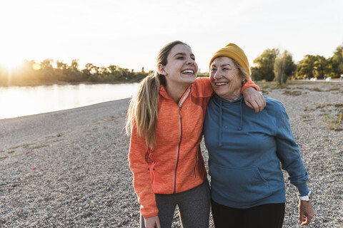 Fit grandmother and granddaughter walking at the river with arms around, having fun stock photo