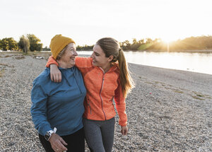 Fit grandmother and granddaughter walking at the river with arms around, having fun - UUF16124