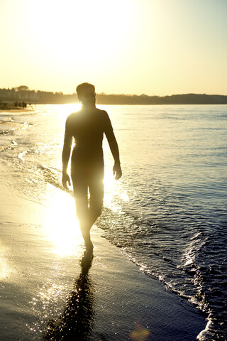 Silhouette eines Mannes, der bei Sonnenuntergang am Strand spazieren geht, lizenzfreies Stockfoto