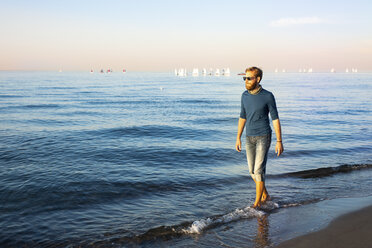 Young man walking at the beach in the evening - PUF01344