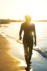 Silhouette eines Mannes, der bei Sonnenuntergang am Strand spazieren geht - PUF01345