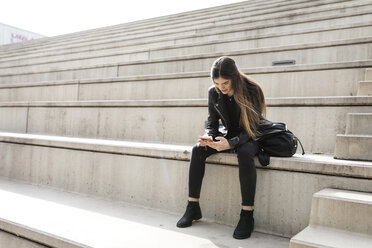 Young woman sitting on stairs using cell phone - VABF01939