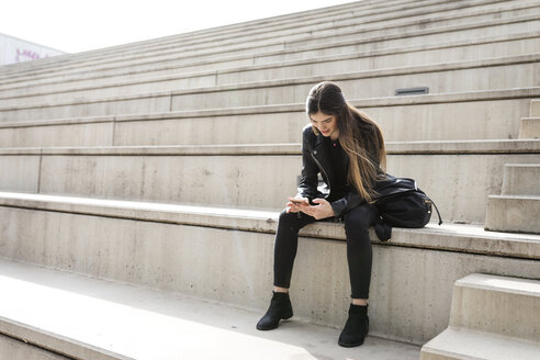 Junge Frau sitzt auf einer Treppe und benutzt ein Mobiltelefon - VABF01939