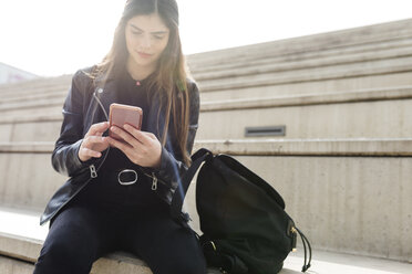 Young woman sitting on stairs using cell phone - VABF01945