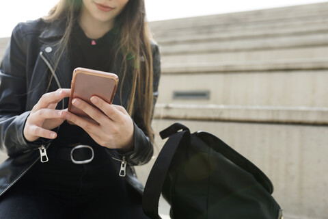 Nahaufnahme einer jungen Frau, die auf einer Treppe sitzt und ein Mobiltelefon benutzt, lizenzfreies Stockfoto