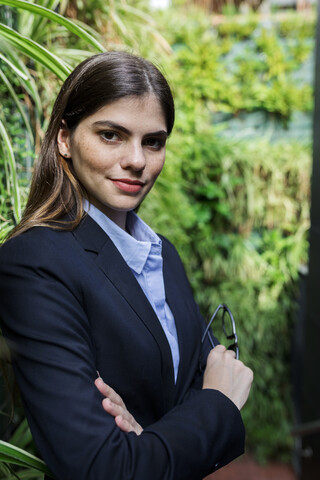 Porträt einer selbstbewussten jungen Geschäftsfrau, umgeben von Pflanzen, lizenzfreies Stockfoto