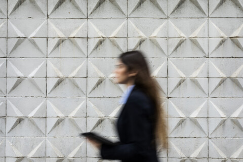 Unscharfe junge Geschäftsfrau hält Tablet vorbei an Betonwand, lizenzfreies Stockfoto
