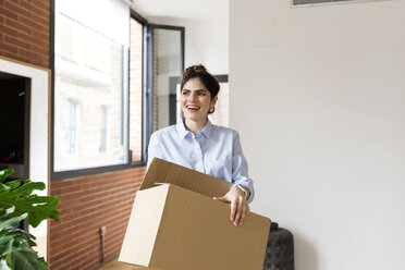 Smiling young woman carrying cardboard box in new apartment - VABF02014