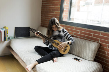 Junge Frau sitzt auf der Couch zu Hause und spielt Gitarre - VABF02027