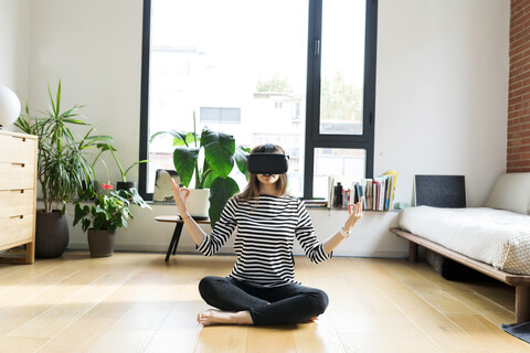 Junge Frau zu Hause mit VR-Brille beim Yoga, lizenzfreies Stockfoto