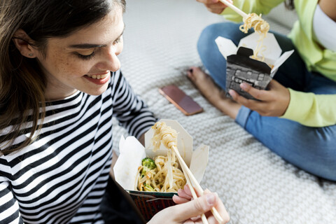 Zwei glückliche junge Frauen essen zu Hause asiatisches Essen zum Mitnehmen, lizenzfreies Stockfoto