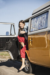 Pretty woman on a road trip with her camper, taking a break, drinking coffee - UUF16145