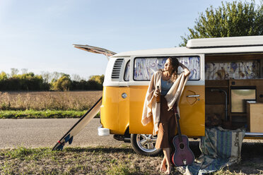 Hübsche Frau auf einem Roadtrip mit ihrem Wohnmobil, trinkt Bier, hält Gitarre - UUF16182