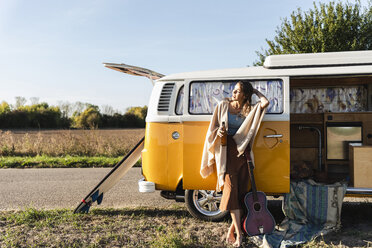 Pretty woman on a road trip with her camper, drinking beer, holding guitar - UUF16182