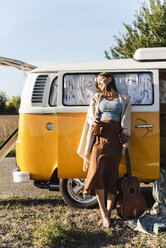 Pretty woman on a road trip with her camper, drinking beer, holding guitar - UUF16185