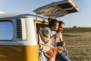 Ein glückliches Paar, das mit seinem Wohnmobil einen Roadtrip macht, auf dem Bett sitzt und Kaffee trinkt - UUF16191