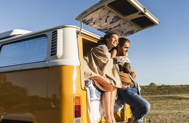 Ein glückliches Paar, das mit seinem Wohnmobil einen Roadtrip macht, auf dem Bett sitzt und Kaffee trinkt - UUF16192