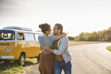 Happy couple doing a road trip with a camper, embracing on the road - UUF16195