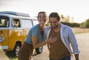 Happy couple doing a road trip with a camper, embracing on the road - UUF16197