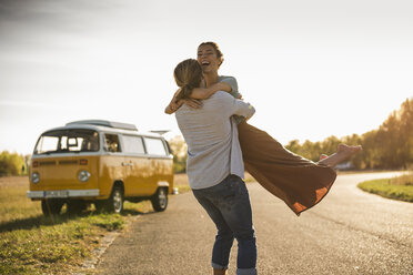 Happy couple doing a road trip with a camper, embracing on the road - UUF16199